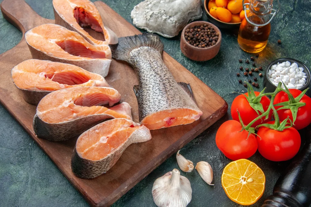 sostituire le proteine della carne col pessce vista dall'alto pesce fresco crudo tagliere di legno bottiglia d'olio alimenti freschi scuro mix di colori tavolo